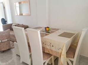 Een eetgedeelte met een tafel voor vier personen, omringd door witte stoelen. Er staat een fruitschaal op de tafel en een spiegel hangt aan de muur.