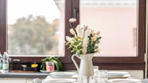 Una mesa de comedor dispuesta con platos, vasos y una jarra blanca con flores.