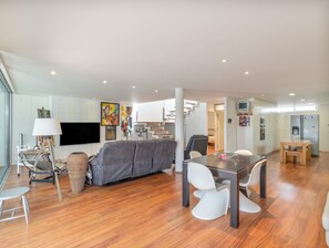 Ein modernes Wohnzimmer mit grauem Sofa, Esstisch und Stühlen, einem Flachbildfernseher und einer Treppe zu einer oberen Ebene.
