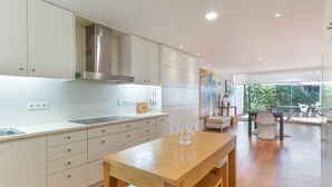 Una cocina moderna con armarios blancos, extractor de acero inoxidable y una mesa de comedor de madera con un centro de mesa de vidrio.