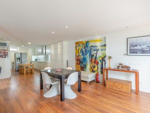 Eine moderne Küche mit Kühlschrank, Esstisch und Stühlen. An der Wand hängt ein großes abstraktes Gemälde und über dem Kamin ein gerahmtes Bild.