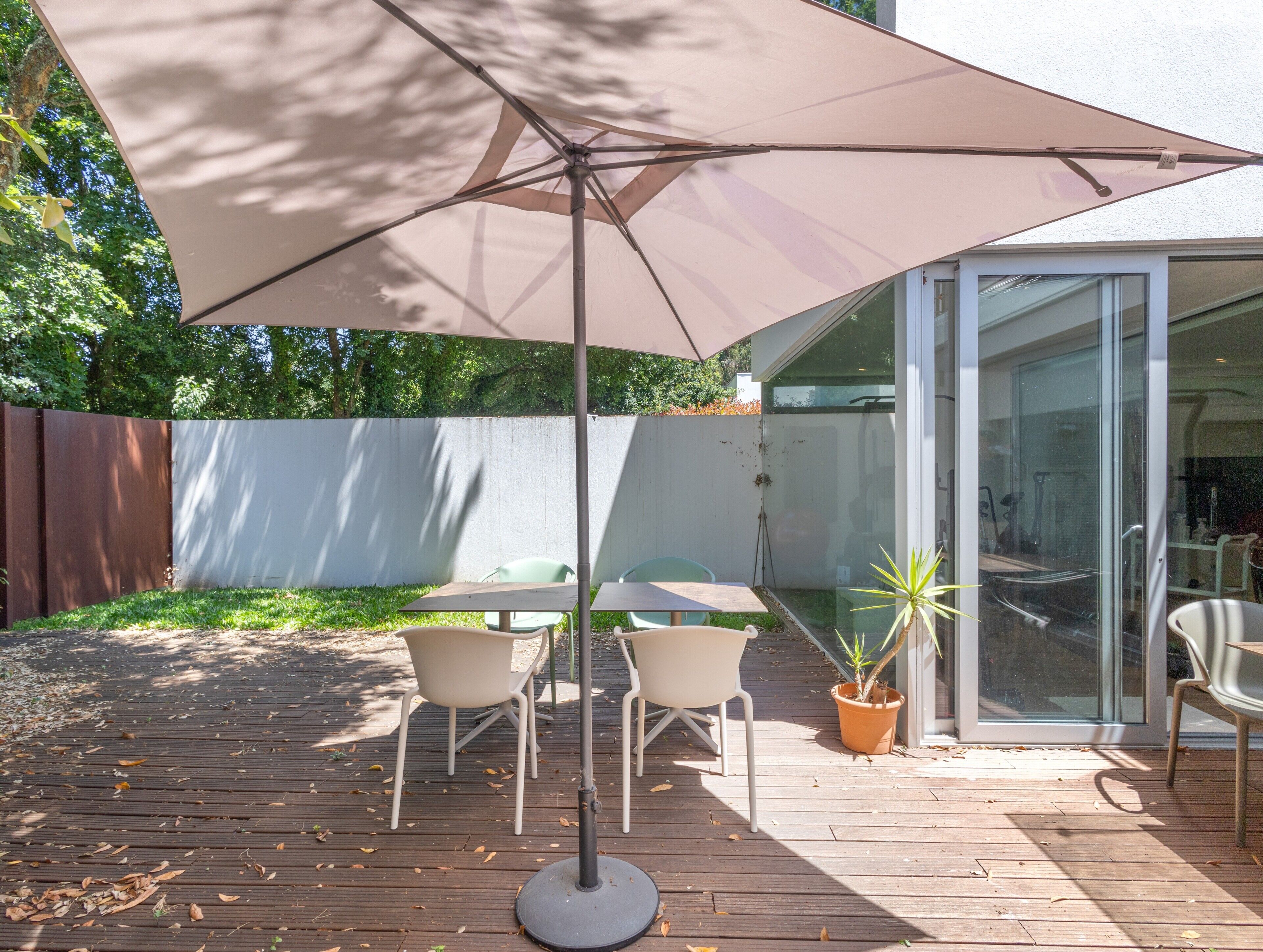 Un patio con una mesa, sillas, una planta en maceta y un ventanal corredero.