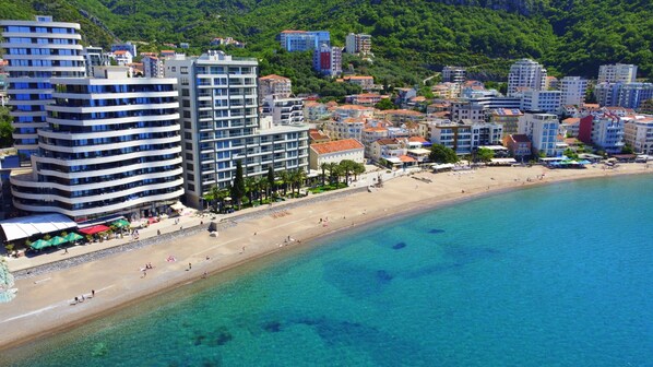 A coastal cityscape with modern buildings, a sandy beach, and clear blue waters.