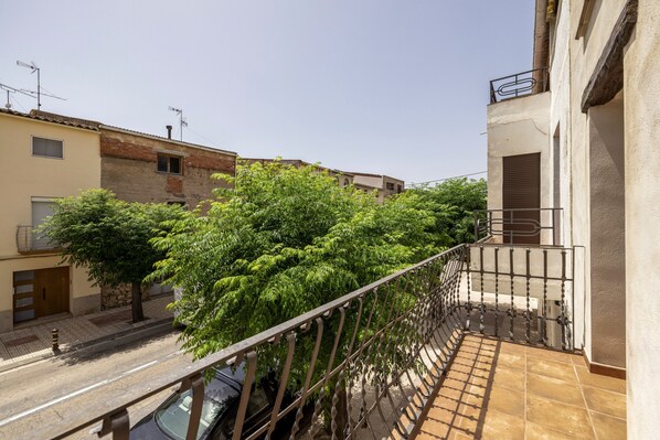 Varanda residencial com grades de metal, uma árvore e um carro estacionado.