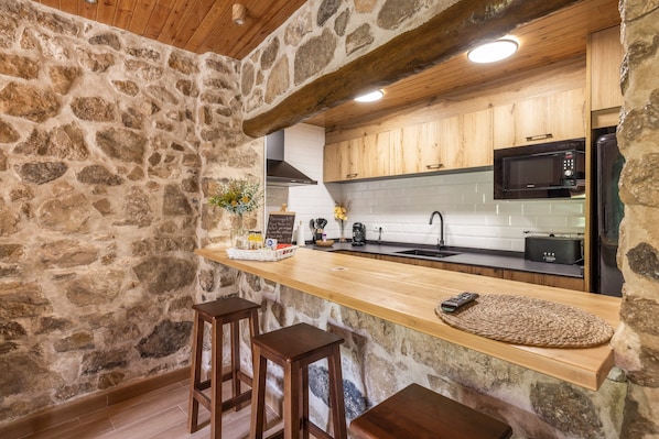 Una cocina de paredes de piedra con taburetes de bar de madera, una encimera de madera y un microondas.