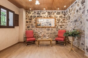 Una habitación con paredes de piedra, techo de madera, dos sillas rojas, una mesita y una planta en maceta.
