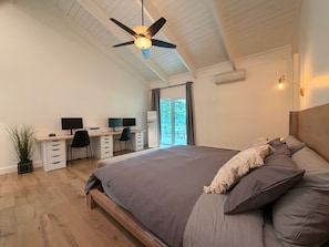 Ein Schlafzimmer mit einem Bett, einem Schreibtisch, zwei Stühlen, einem Deckenventilator und einem Fenster.