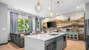 Een moderne keuken met een centraal eiland, inbouwapparatuur en een groot raam met gordijnen.