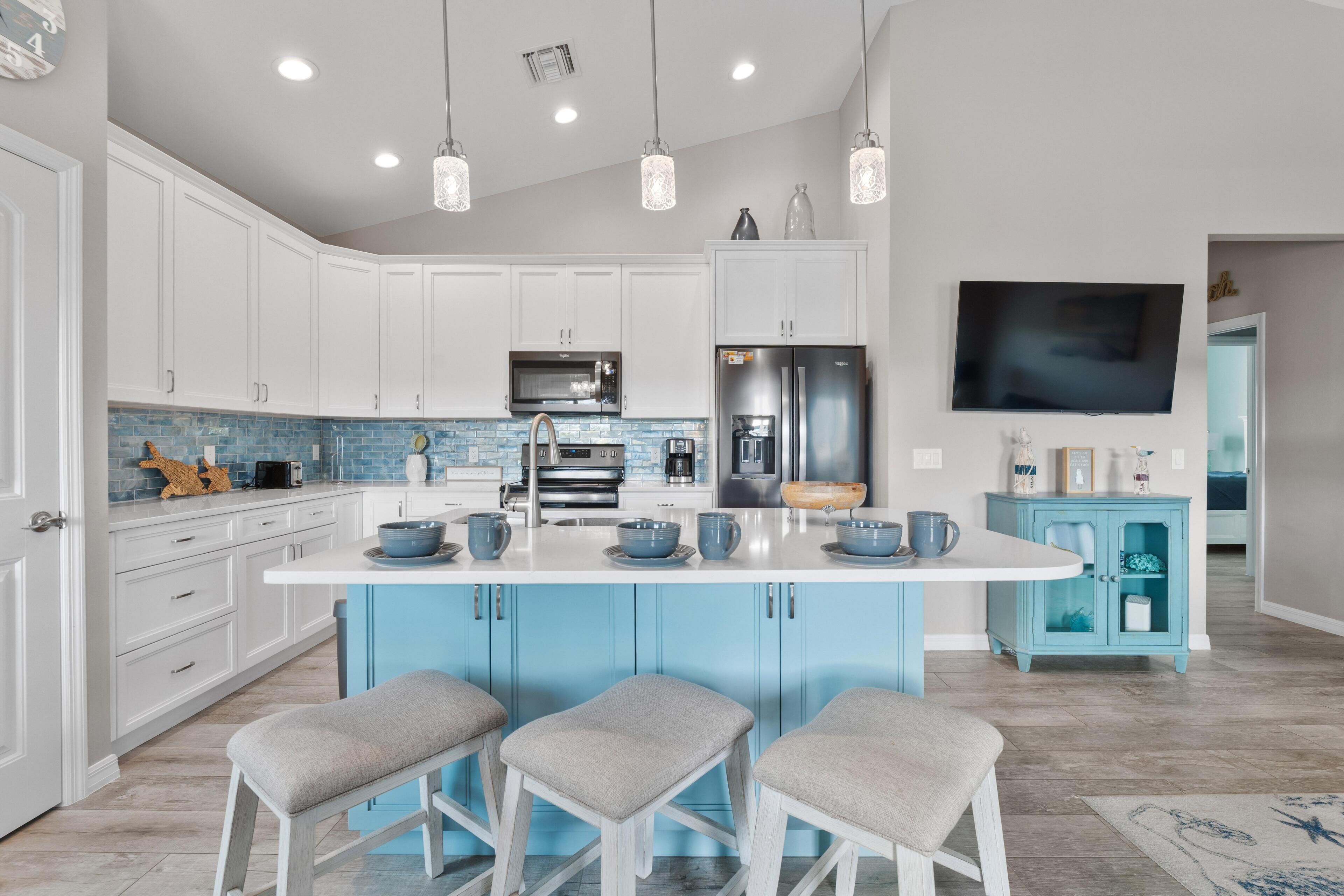 Una cucina moderna con mobili bianchi, un'isola blu e una grande TV montata a parete.