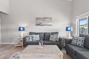 Ein Wohnzimmer mit einem grauen Sofa, einem Couchtisch mit Schiffverzierung und einem Gemälde einer Brücke an der Wand.
