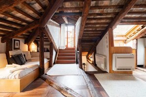 Ein schmales Schlafzimmer im Dachgeschoss mit einer Holztreppe, einem Bett und einem Heizkörper.
