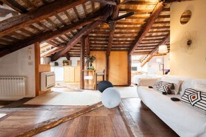 Ein Dachzimmer mit freiliegenden Holzbalken, einem weißen Sofa und einem Deckenventilator.