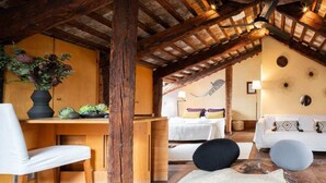 Ein rustikaler Raum mit freiliegenden Holzbalken, einem Holztisch, einem weißen Sofa und einem Bett mit gemusterten Kissen.