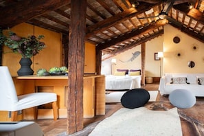 Ein rustikaler Raum mit freiliegenden Holzbalken, einem Holztisch, einem weißen Sofa und einem Bett mit gemusterten Kissen.