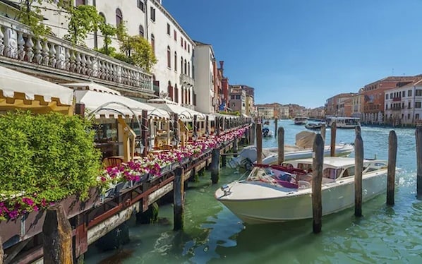 Ein Restaurant am Kanal mit Außenbereich, ein Boot liegt in der Nähe, und Gebäude säumen das Wasser.