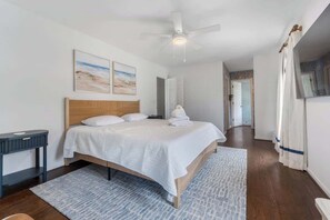 A bedroom with a bed, a bedside table, a ceiling fan, and a hallway leading to another room. - 704 at the Shore! Pet Friendly and Close to Beach (Kure Beach)