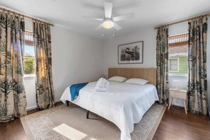 Une chambre à coucher avec un lit, un ventilateur de plafond, une table de chevet et des rideaux.