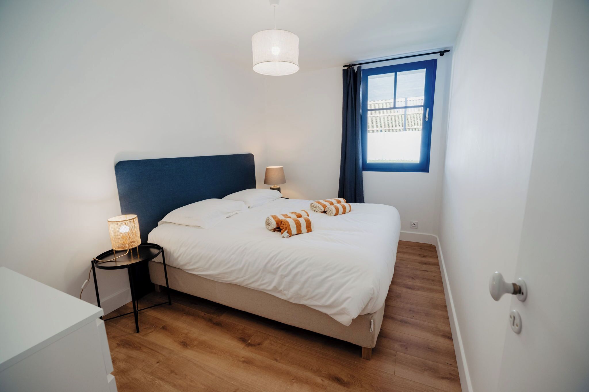 A bedroom with a bed, a bedside table with a lamp, a window with curtains, and a door.