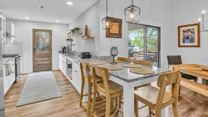 A modern kitchen with a central island, wooden chairs, and pendant lighting. - The Good Life OKI | Hot Tub & Game Room (Oak Island)