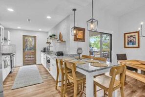 A modern kitchen with a central island, wooden chairs, and pendant lighting. - The Good Life OKI | Hot Tub & Game Room (Oak Island)