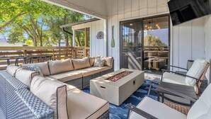 A covered outdoor seating area with a sofa, chairs, and a fire pit. - The Good Life OKI | Hot Tub & Game Room (Oak Island)