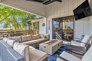 A covered outdoor seating area with a sofa, chairs, and a fire pit. - The Good Life OKI | Hot Tub & Game Room (Oak Island)