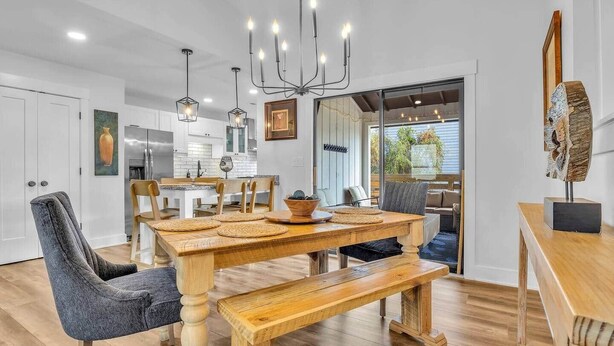 A modern kitchen with white cabinets, a dining area with a wooden table and chairs, and a chandelier. - The Good Life OKI | Hot Tub & Game Room (Oak Island)