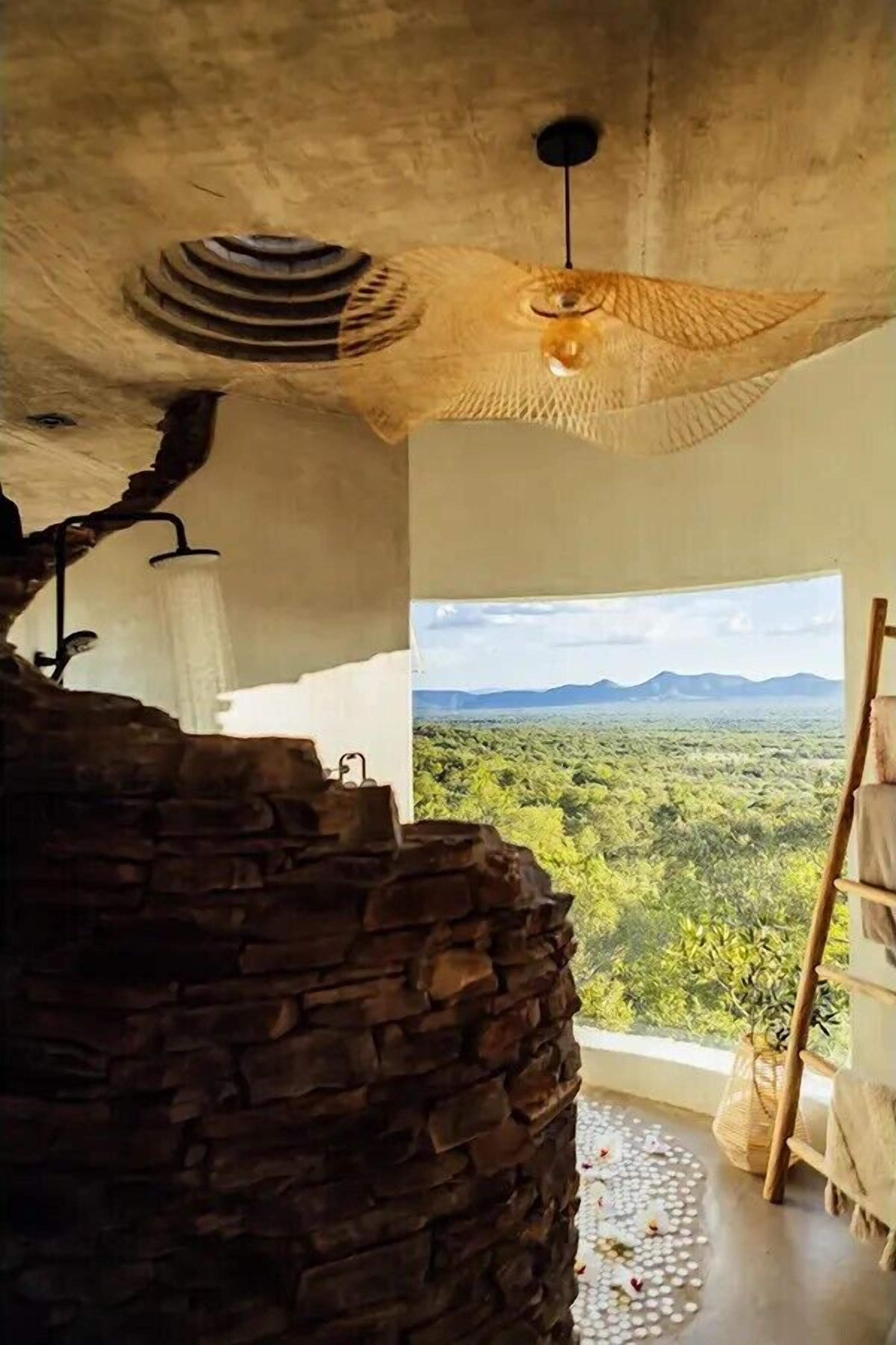 A room with a stone wall, a hanging light fixture, and a view of a green landscape through a window.