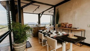Un área de comedor con vistas, que incluye una mesa, sillas, una planta en maceta y una obra de arte en la pared.