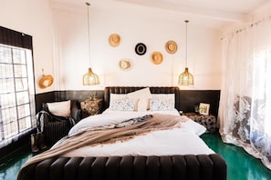 A bedroom with a large bed, a chair, a nightstand, and a wall with decorative hats.