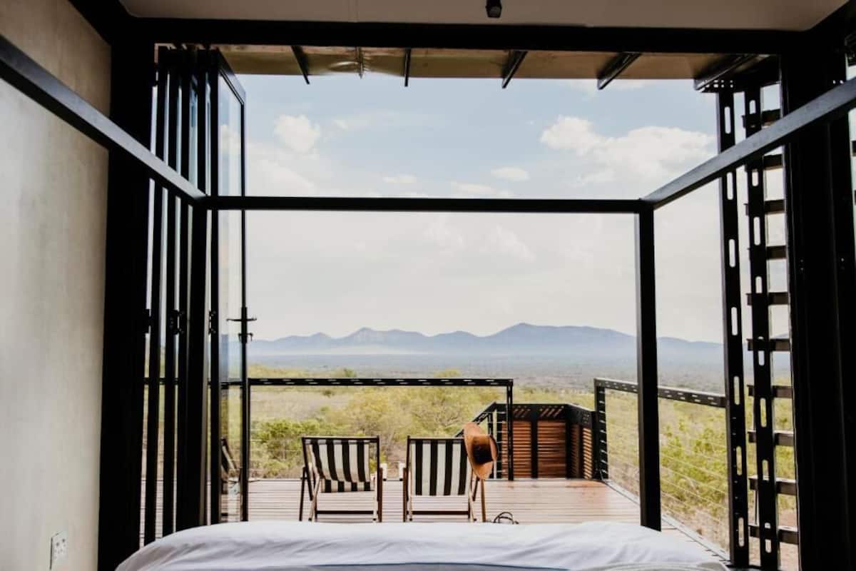 A room with a bed, two striped chairs, and a view of a mountainous landscape.