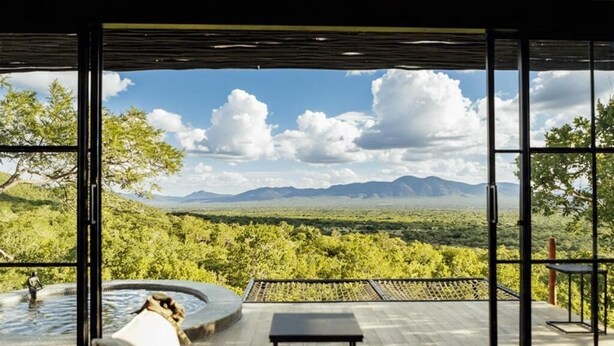 Una habitación moderna con un ventanal grande, un jacuzzi y vistas a un paisaje montañoso.