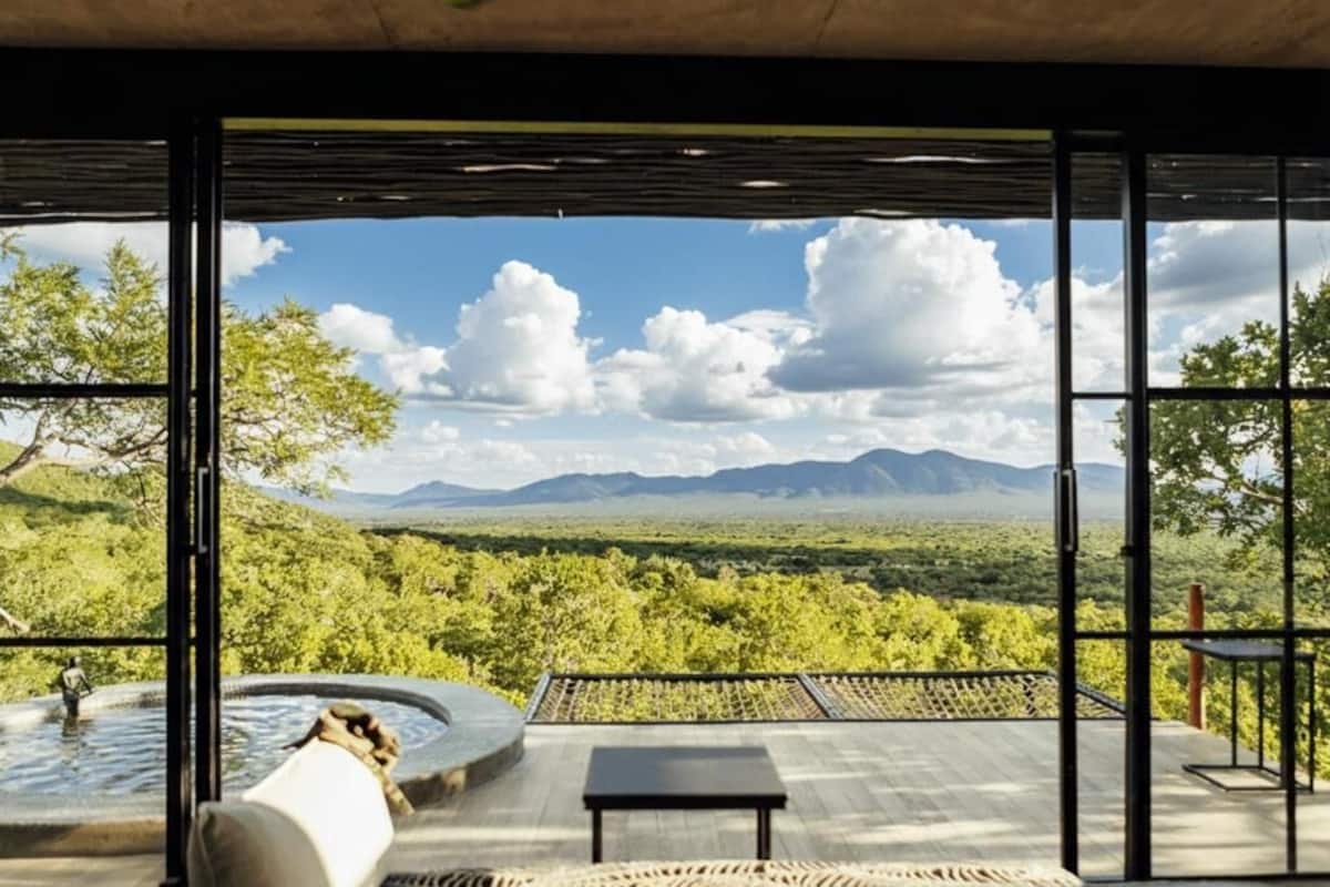A modern room with a large window, a hot tub, and a view of a mountainous landscape.