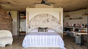 Un dormitorio con cama con dosel, ventilador de techo, pared de ladrillo, kitchenette y una zona de estar.
