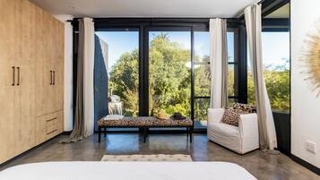 Quarto moderno com uma cama grande, um sofá e vista para o verde através de janelas do chão ao teto.