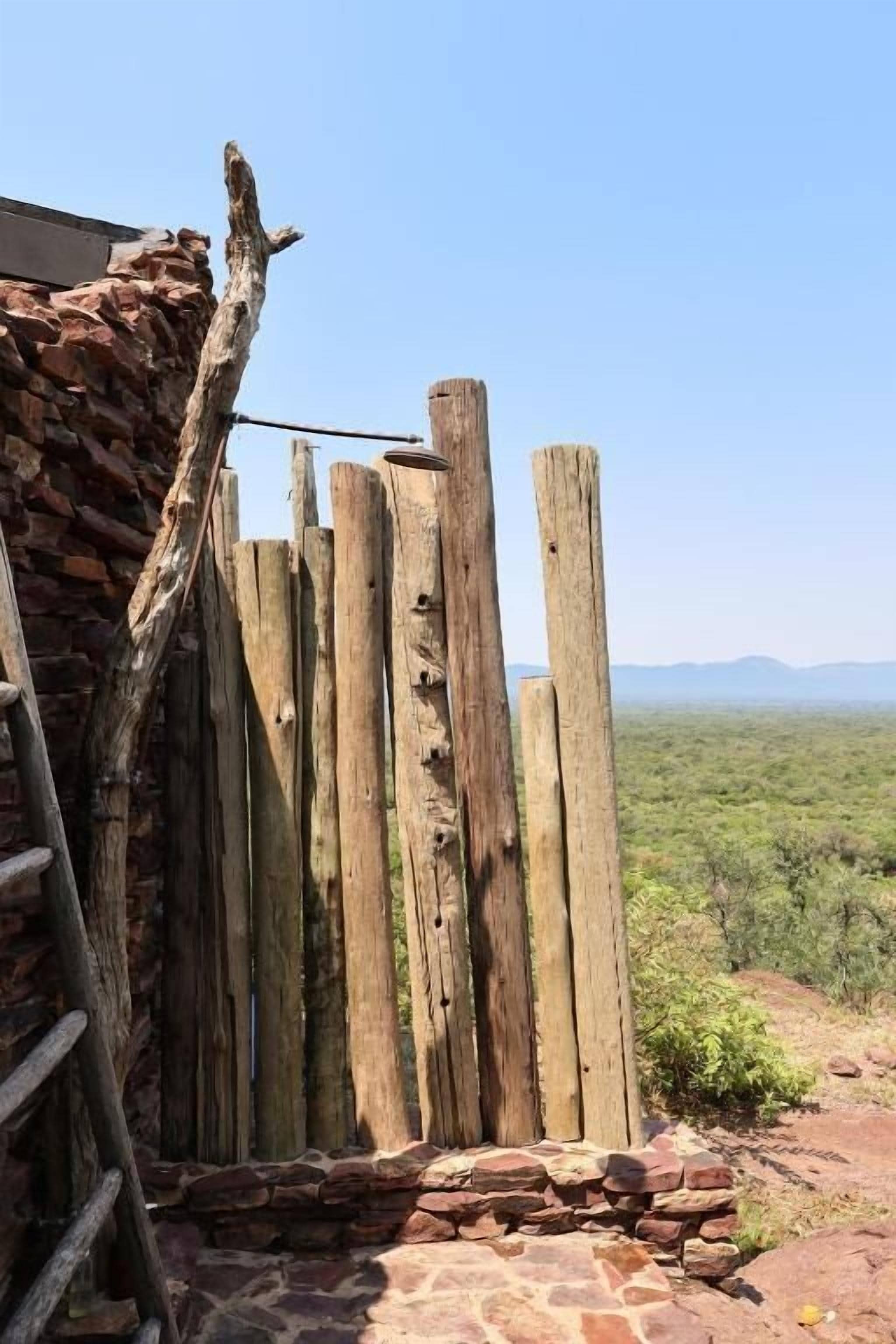 A rustic wooden fence with a stone wall, a ladder, and a clear view of a hilly landscape.