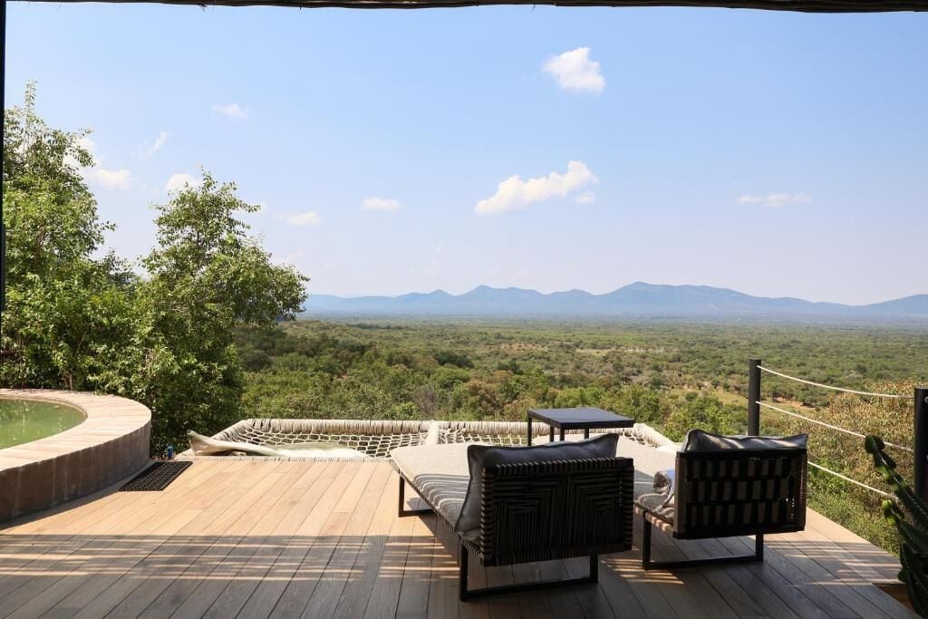 Una terraza con una hamaca, dos sillas y una mesita con vista a un paisaje montañoso.
