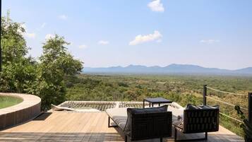 Una terraza con una hamaca, dos sillas y una mesita con vista a un paisaje montañoso.