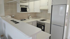 Une cuisine compacte équipée d’un four à micro-ondes, d’une cuisinière et d’un réfrigérateur, avec des meubles blancs et un dosseret carrelé.