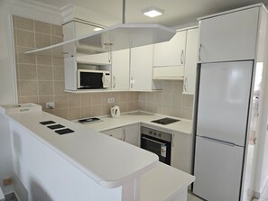 Eine kompakte Küche mit Mikrowelle, Herd und Kühlschrank, mit weißen Schränken und einer gefliesten Spritzschutzwand.