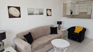 Un salon avec un canapé beige, une petite table blanche, un fauteuil noir et des œuvres d’art accrochées au mur.