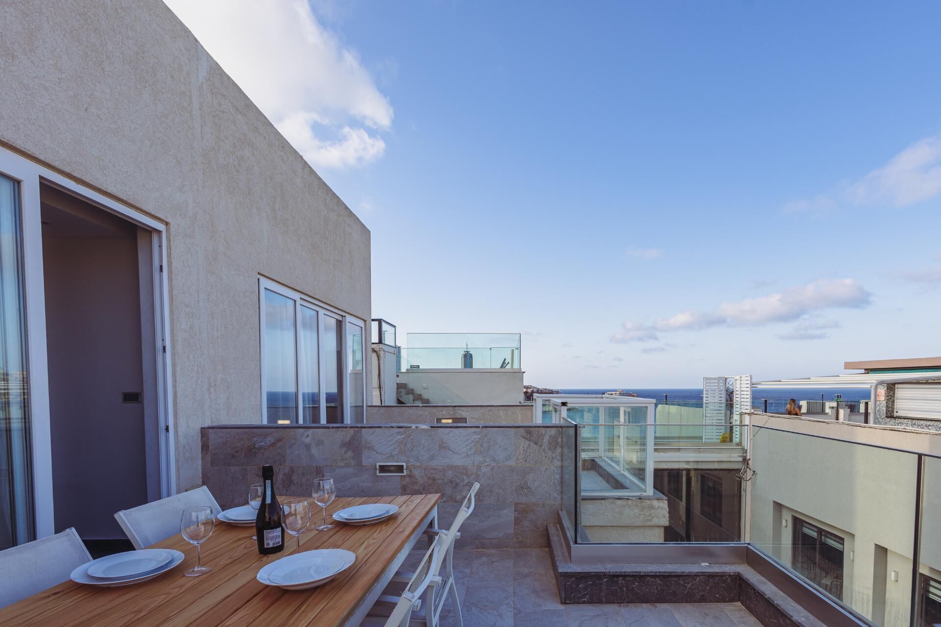 A rooftop terrace with a dining table set for two, a bottle of wine, and a clear view of the sea.