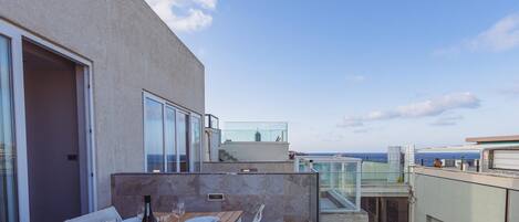 A rooftop terrace with a dining table set for two, a bottle of wine, and a clear view of the sea.