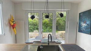 Eine moderne Küche mit einem großen Fenster, einem Spülbecken und einem Essbereich, der durch Glastüren sichtbar ist.