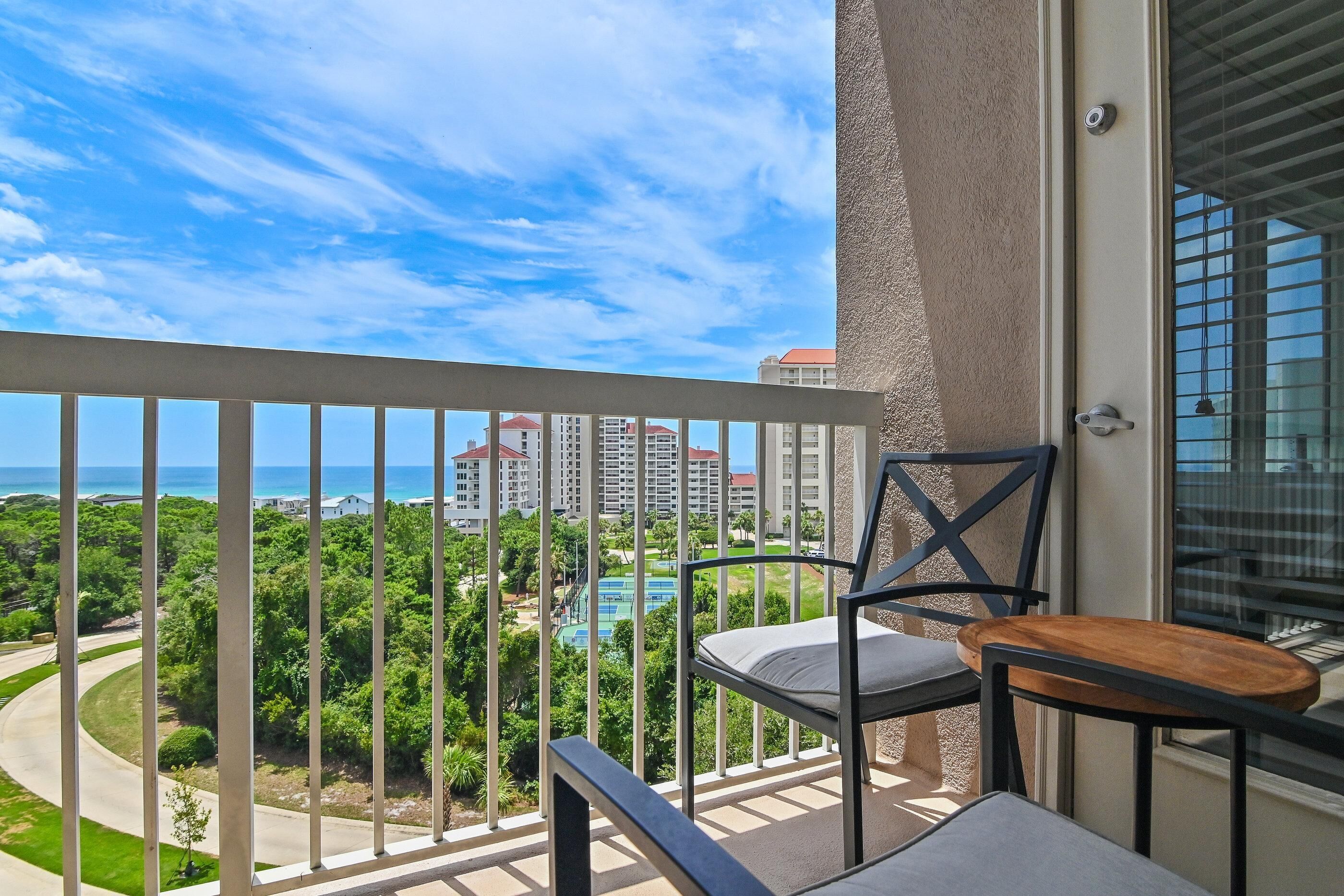 A balcony with a view of a swimming pool, greenery, and buildings.
