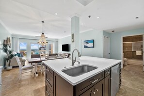 A modern kitchen with a central island, a dining area with a view, and a living space with a large window. - Summit at Tops'l 612- Miramar Memories (Miramar Beach)