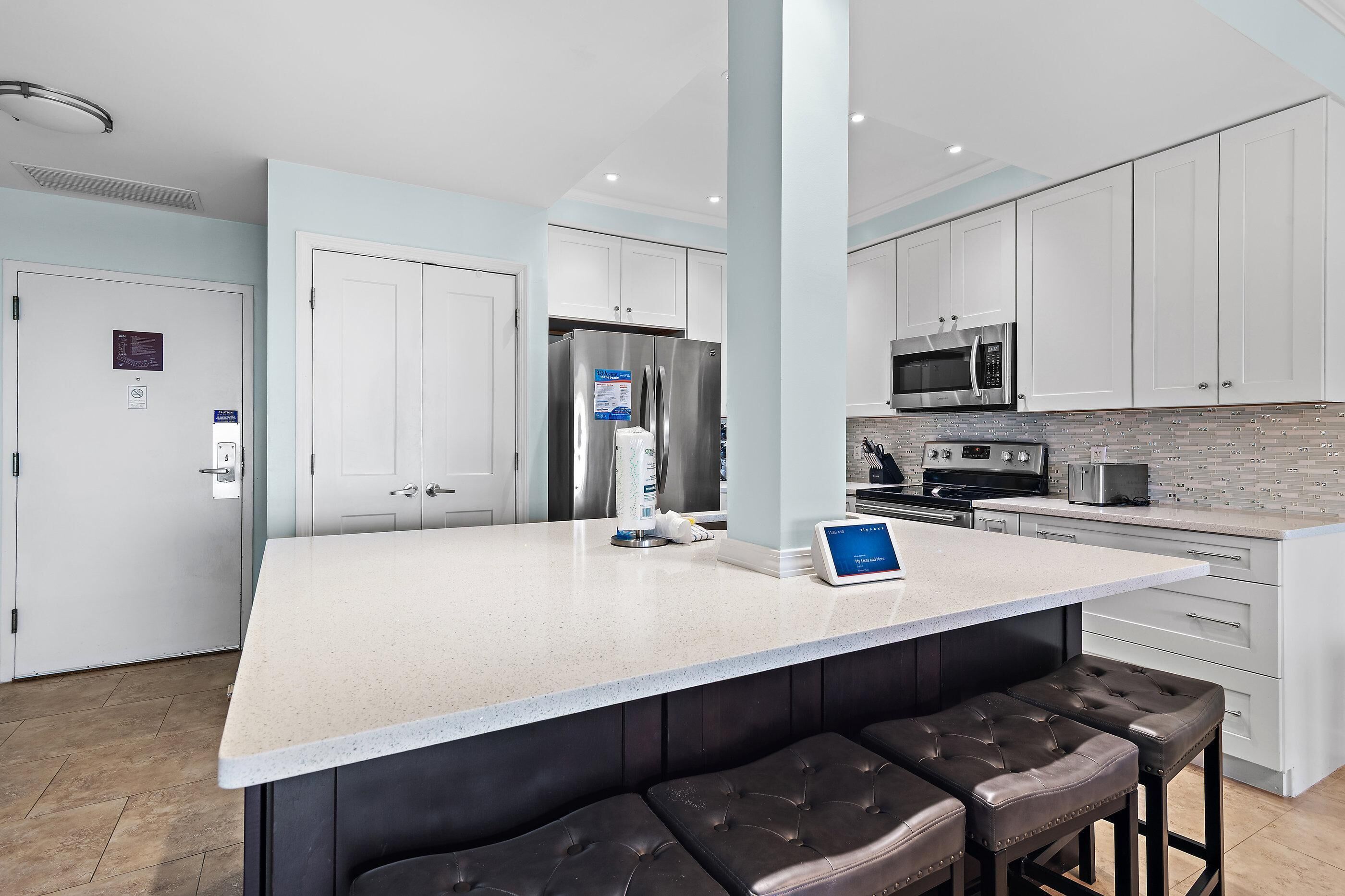 A modern kitchen with white cabinets, stainless steel appliances, a central island with bar stools, and a digital clock displaying the time.