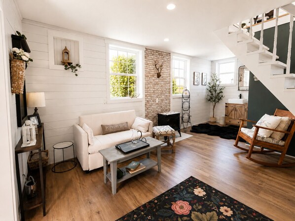 A living room with a white sofa, a coffee table, a fireplace, a staircase, and a wooden floor.