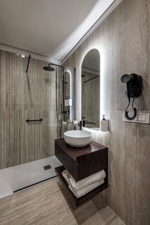 A modern bathroom with a large mirror, a sink, a shower, and a hairdryer mounted on the wall. - VillaFranca Suites Guest House (Roma)
