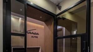 Entrada de hotel con diseño moderno, que incluye una puerta corredera, una zona de recepción con un cartel y una cámara de seguridad.